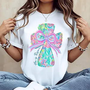 casual round-neck short-sleeve summer T-shirt with vibrant cross and bow design "He Is Risen" printed graphic tee machine washable not dry cleanable made in USA